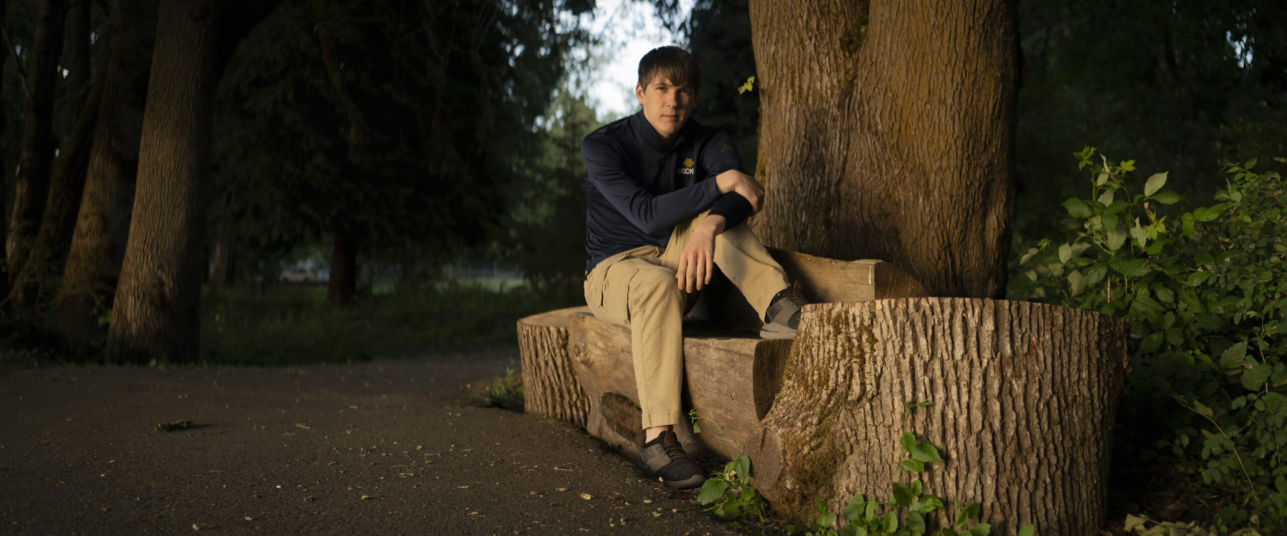 Andrew Boggess sits on a log bench posing for a photo.